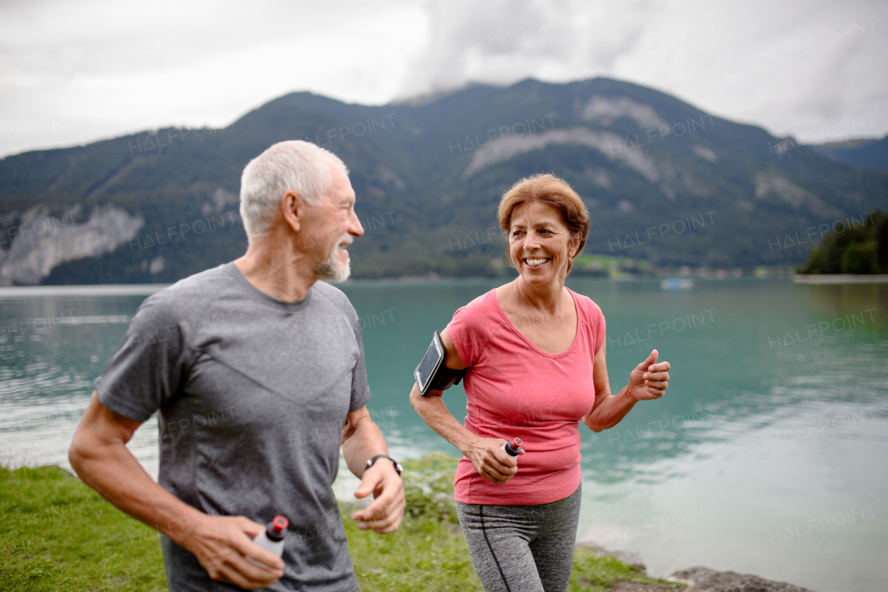 Senior couple running by the lake in nature. Elderly husband and wife spending active vacation in the mountains, enjoying physical activity and relaxation outdoors.