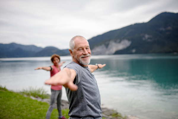 Senior couple doing outdoor yoga, tai chi, pilates by the lake in the autumn. Elderly husband and wife spending active vacation in the mountains. Pensioners stretching after outdoor workout.