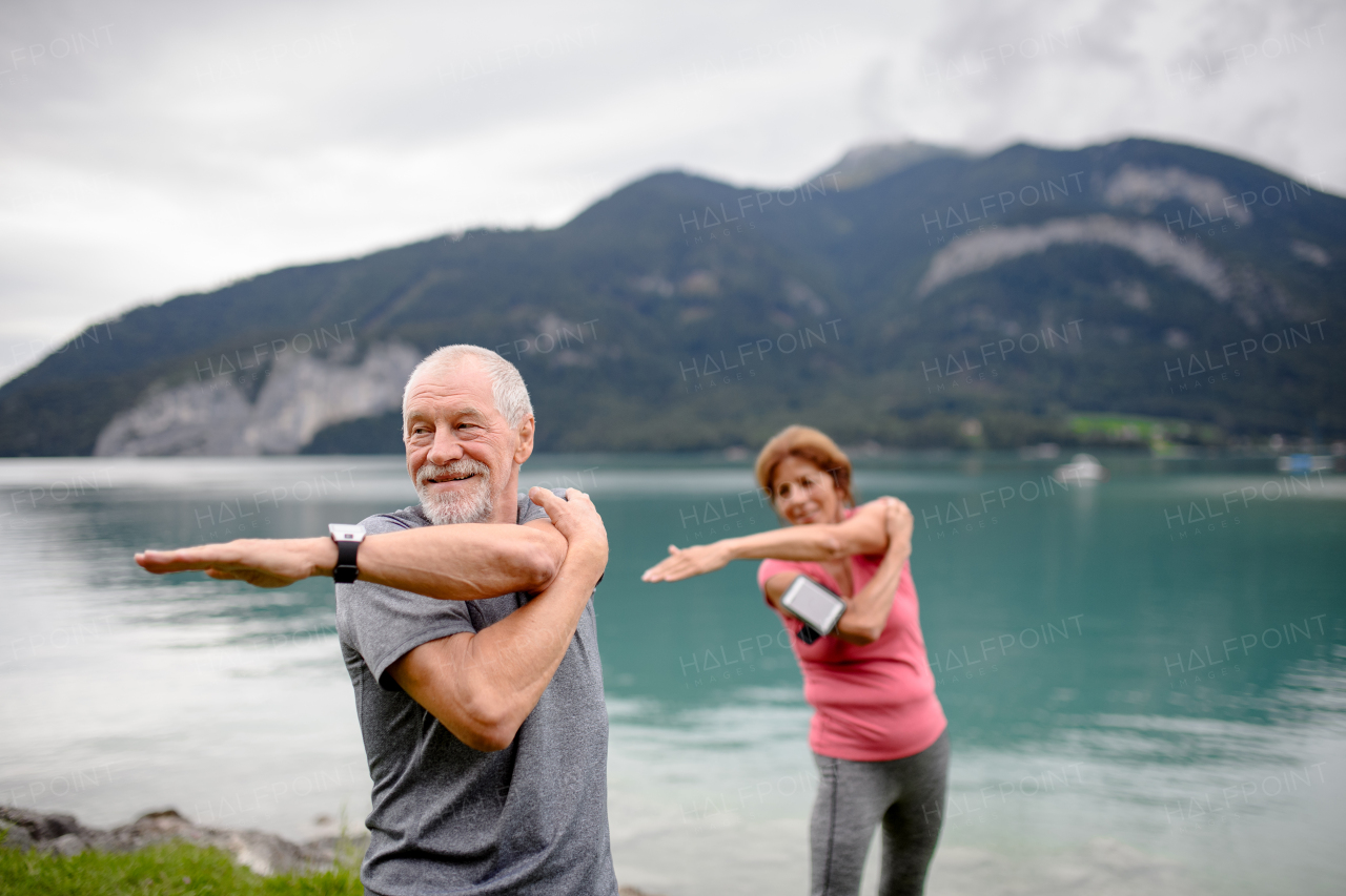 Senior couple doing outdoor yoga, tai chi, pilates by the lake in the autumn. Elderly husband and wife spending active vacation in the mountains. Pensioners stretching after outdoor workout.