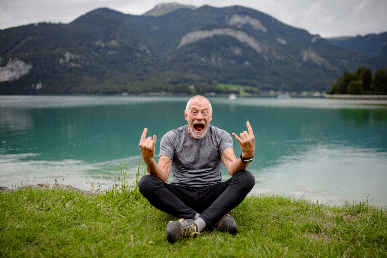 Active senior man is thrilled to accomplish challenging hiking trail. Happy elderly man resting on the grass.