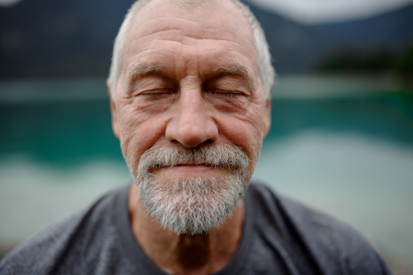 Portrait of active senior man resting after hiking in mountains. Thoughtful elderly man enjoying peaceful untouched nature.