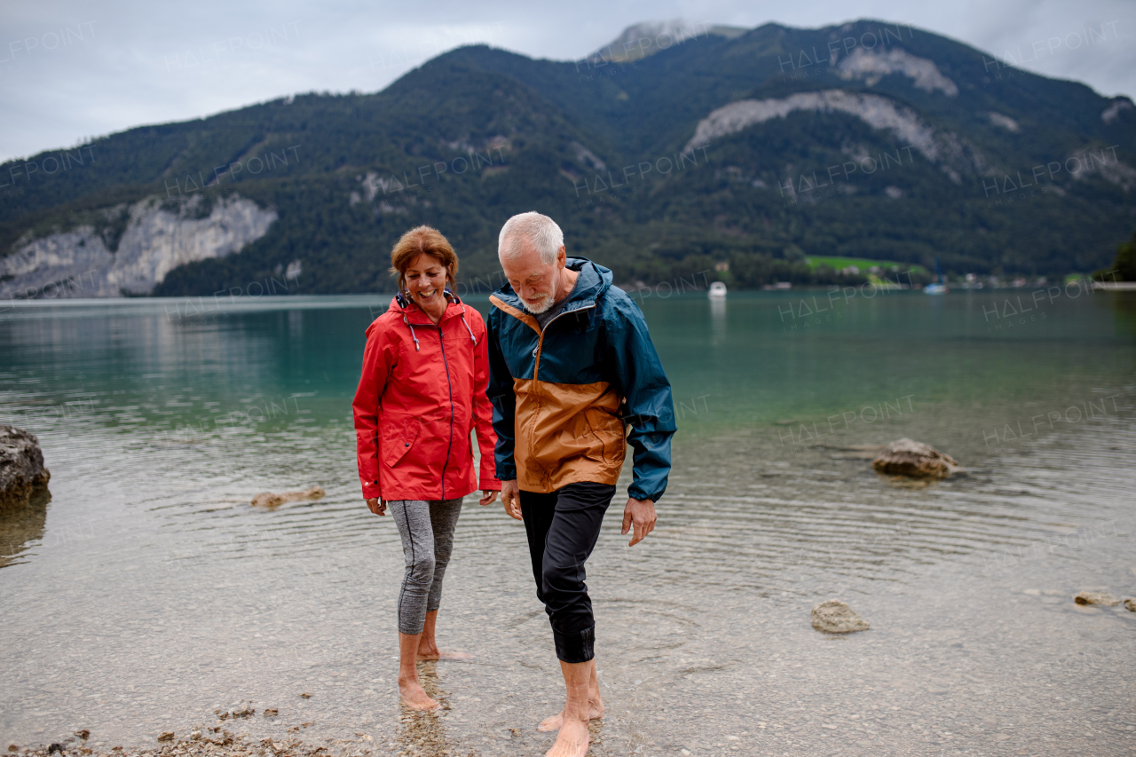 Active elderly couple hiking together in spring mountains, walking in cold fresh water in mountain lake. Senior tourists enjoying nature.