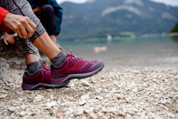 Close up of active woman putting on hiking boots or trail shoes on shore of mountain lake. Senior tourists enjoying nature during early spring.