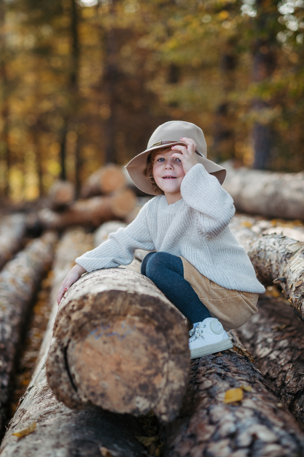 Cute girl with hat sitting on logs in the middle autumn forest, having fun and laughing