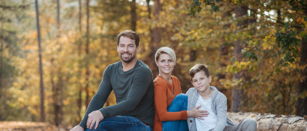 Portrait of family sitting in the middle autumn forest. Nuclear family spending weekend outdoors