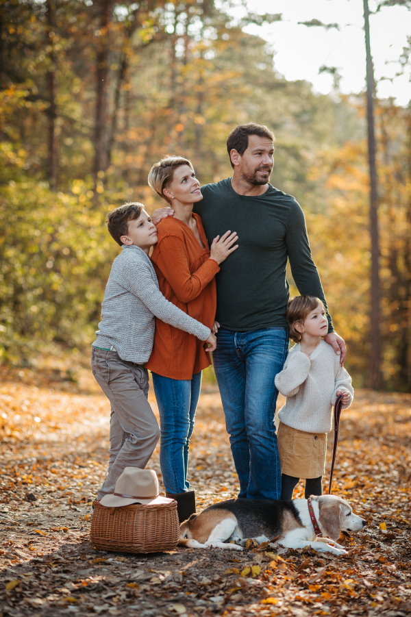 Portrait of young family with two kids and dog on a walk in autumn forest and mushroom hunting.