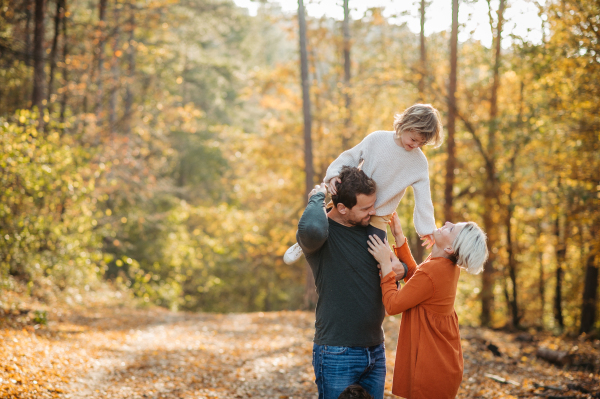 Young family with small children on walk in autumn forest. Father carrying daughter on his shoulders