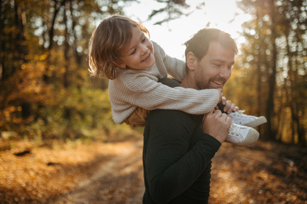 Father and girl are playful during walk in autumn forest. Dad and girl having fun outdoors