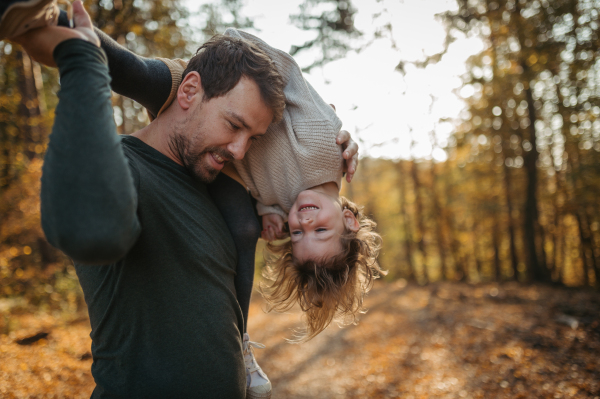 Father and girl are playful during walk in autumn forest. Dad and girl having fun outdoors