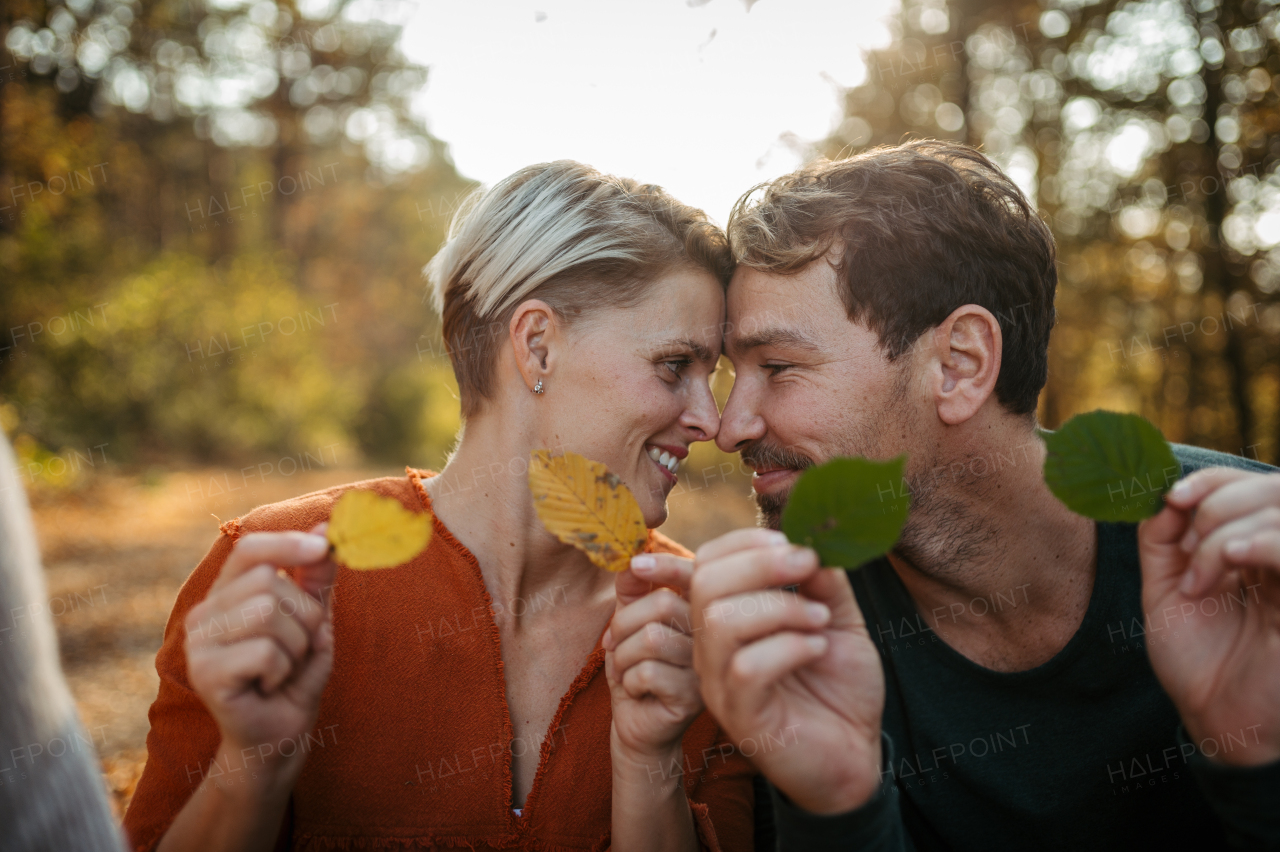 Couple holding colorful leaves, looking at camera. Man and woman on walk in autumn forest