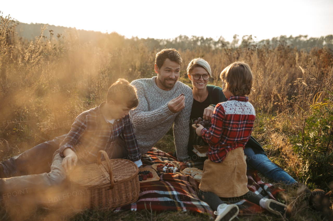 Portrait of family with two kids having picnic in autumn nature, eating fruits and cheese