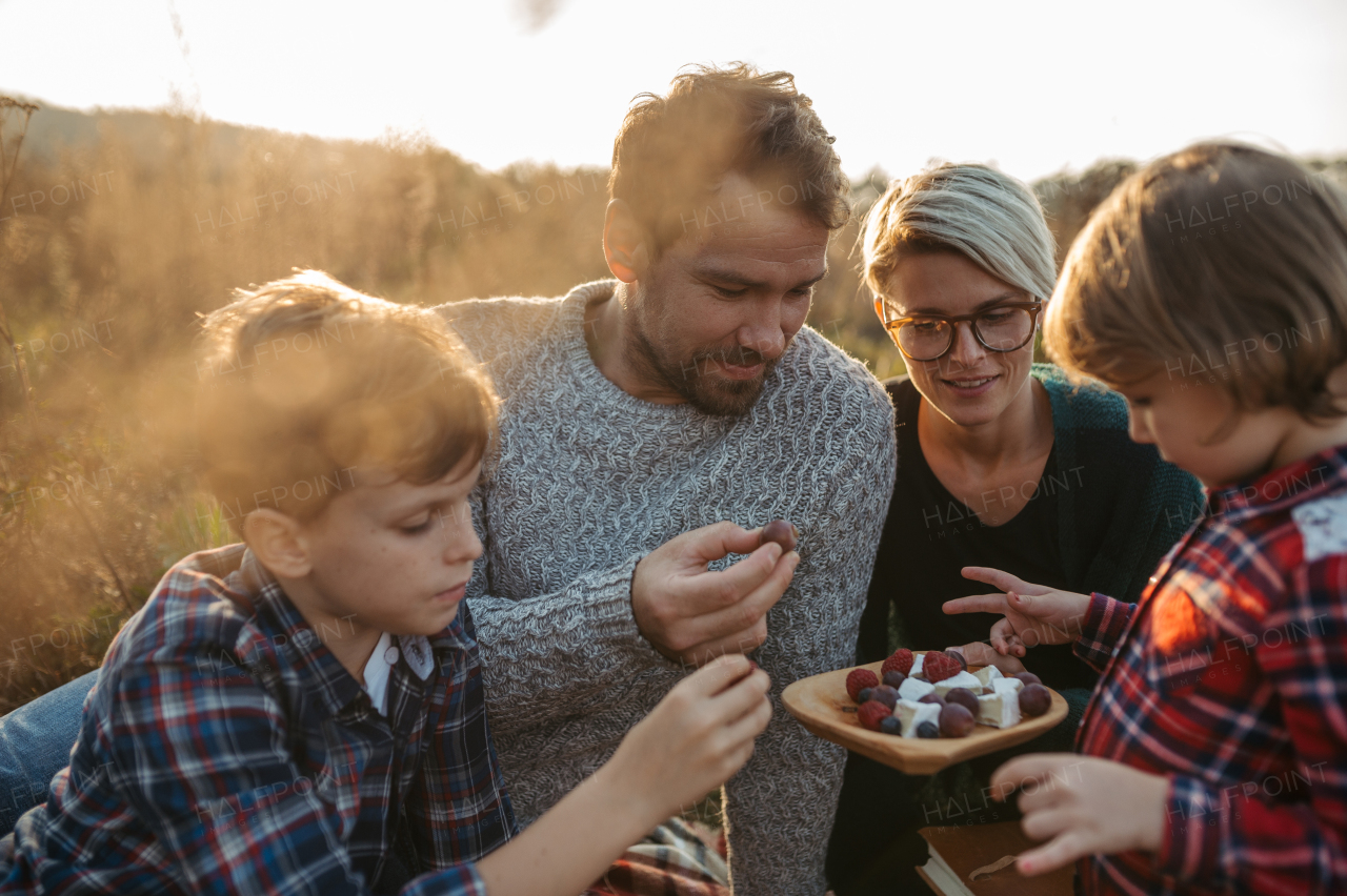 Portrait of family with two kids having picnic in autumn nature, eating fruits and cheese