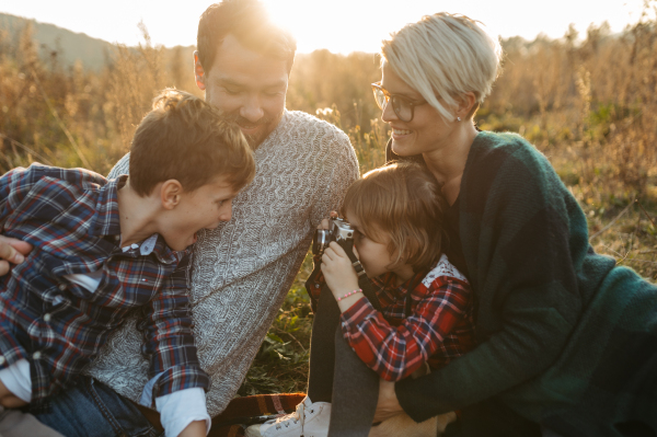 Portrait of family having picnic in autumn nature, eating homemade food in the middle of meadow. Young girl taking pictures with vintage camera