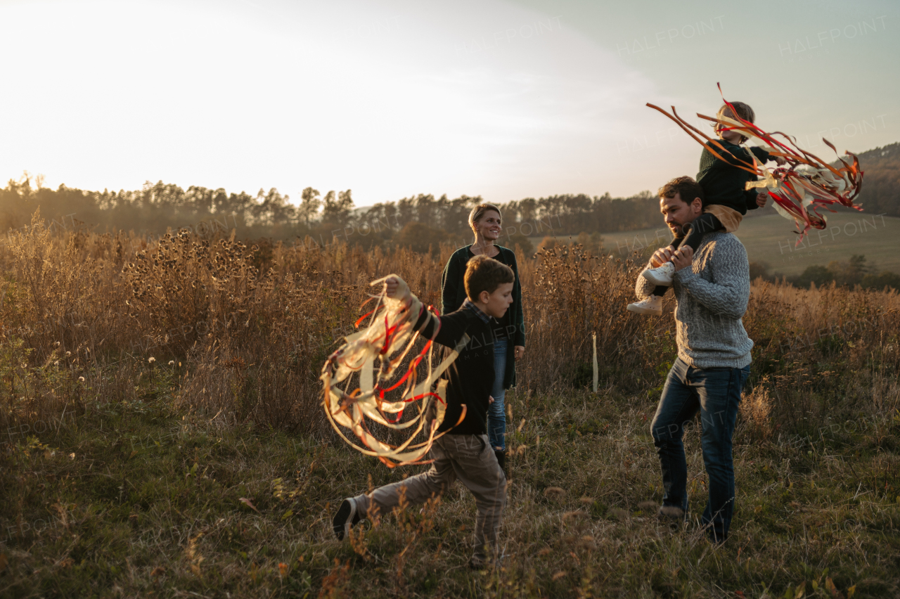 Portrait of young family flying a kite in the autumn nature, jumping in the middle meadow during sunset. Indian summer