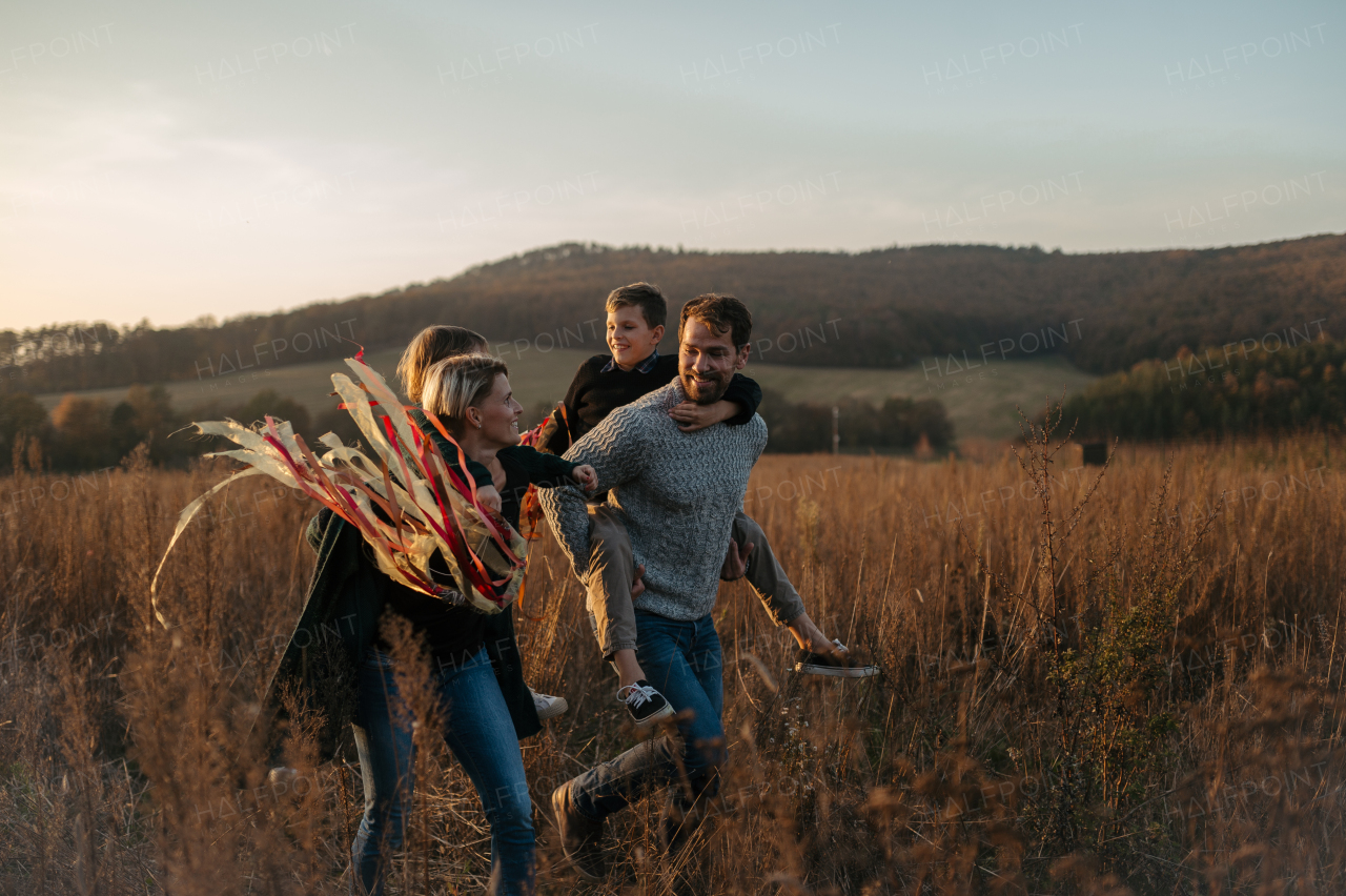 Portrait of young family flying a kite in the autumn nature, jumping in the middle meadow during sunset. Indian summer