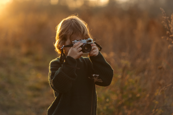 Portrait of cute girl taking photos with vintage camera in the middle of autumn meadow