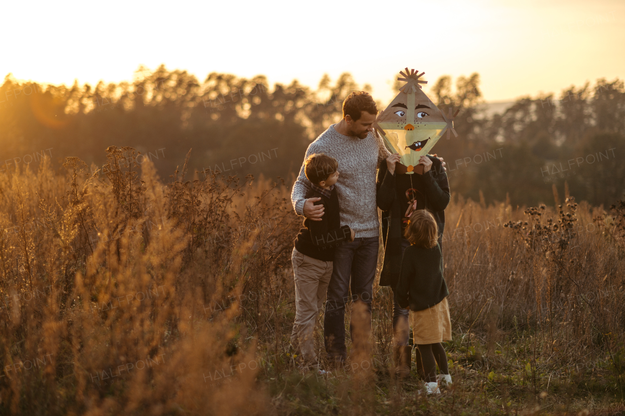 Portrait of young family flying a kite in the autumn nature, jumping in the middle meadow during sunset. Indian summer