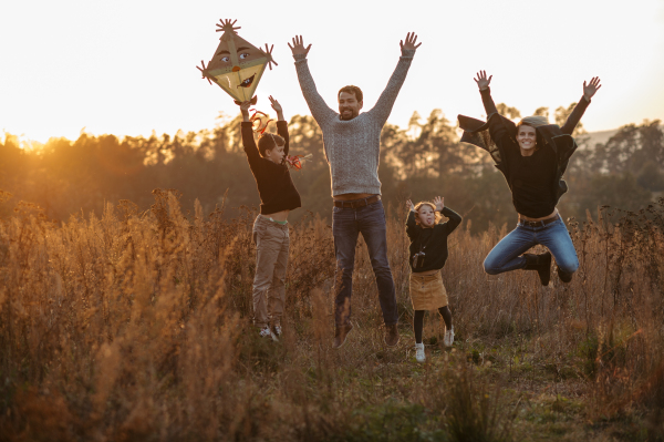 Portrait of young family flying a kite in the autumn nature, jumping in the middle meadow during sunset. Indian summer