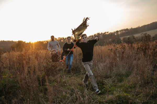 Portrait of young family flying a kite in the autumn nature, jumping in the middle meadow during sunset. Indian summer