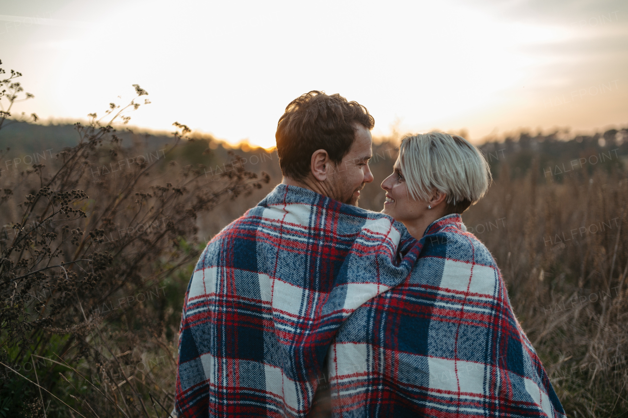 Couple in love on a walk in autumn forest. Husband sitting in meadow with wife covered in warm blanket