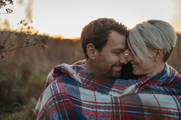 Couple in love on a walk in autumn forest. Husband and wife standing in the middle of meadow covered in warm blanket