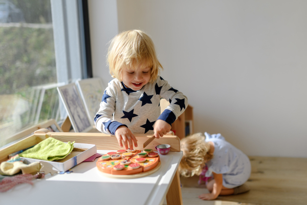 Kids playing with wooden toys in living room, serving and cutting pizza. Siblings spending weekend day indoors.