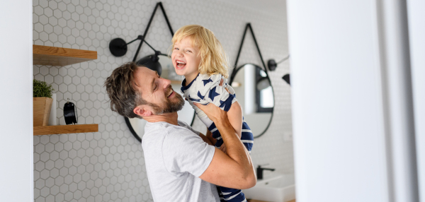 Father holding son in his arms, standing in bathroom. Morning routine for young boy before going to preschool.