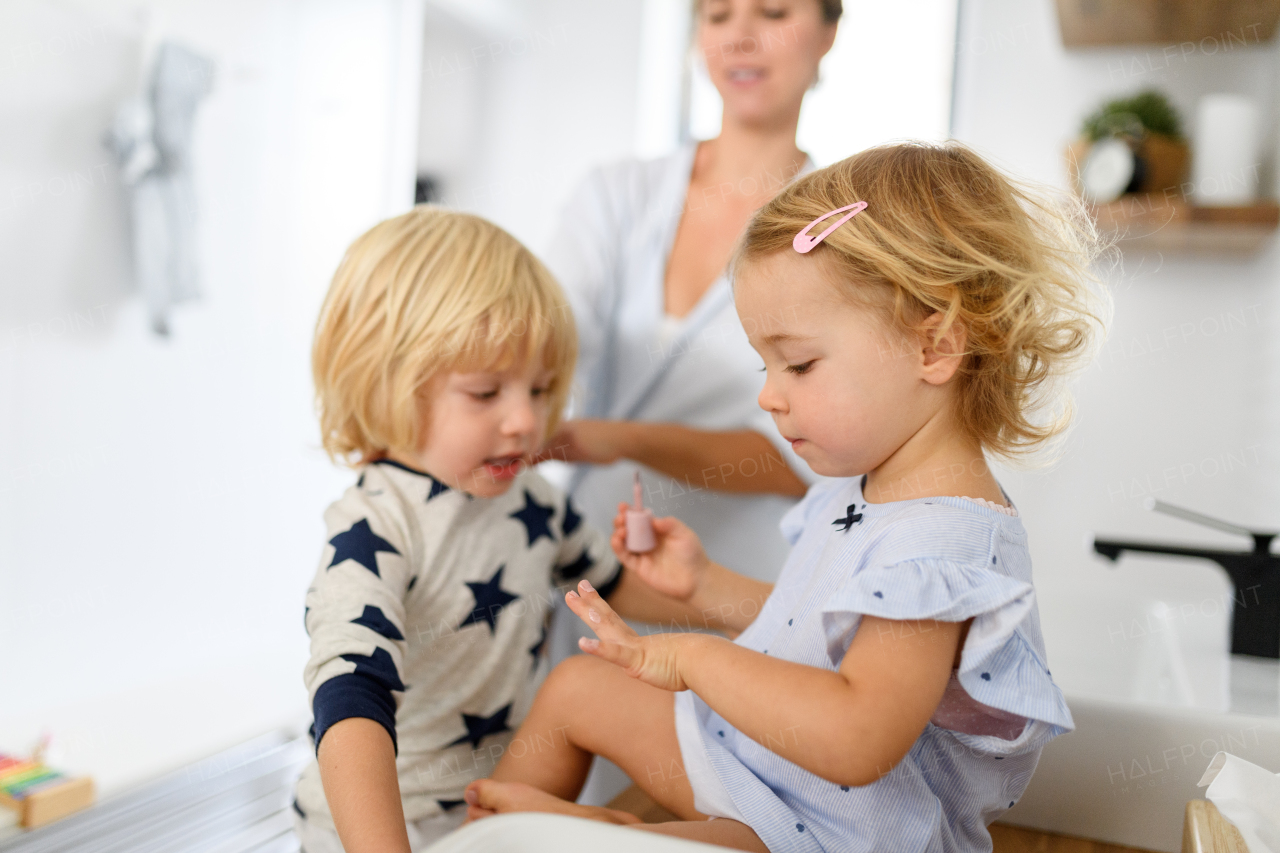 Morning bathroom routine for small children. Girl painting her nails with mom's nail polish, brother looking.