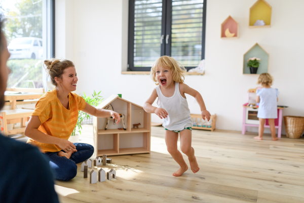 Young nuclear family playing with toys in a living room. Parents and children running, having fun, spending weekend day indoors.