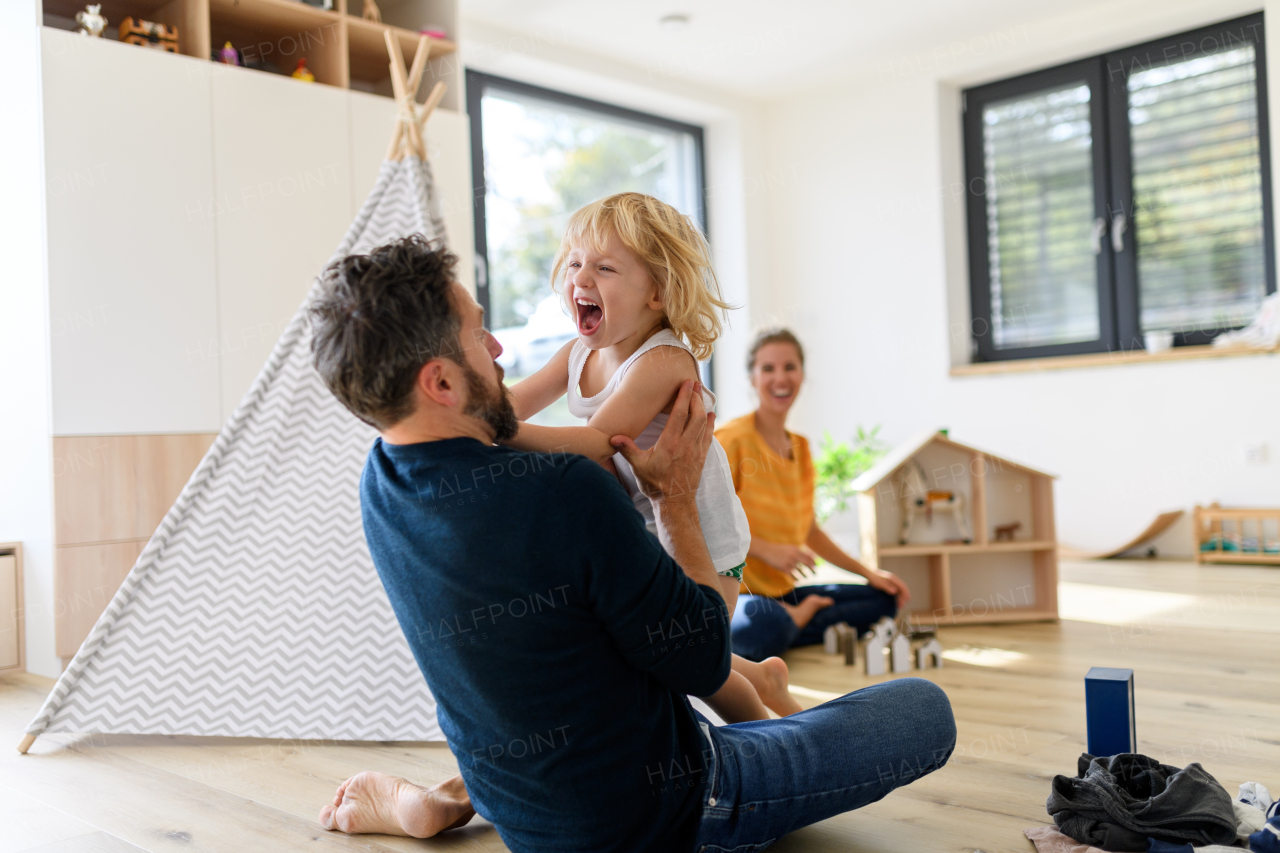 Father putting clothes on small boy, who trying to run off, refusing, screaming. Young nuclear family having fun at home, spending weekend day indoors.