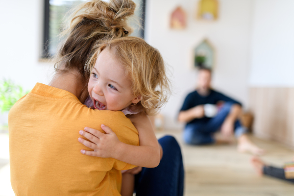 Mom hugging small girl, who trying to run off. Nuclear family having fun at home, spending weekend day indoors.