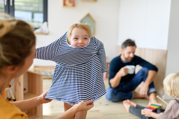 Mom putting clothes on small girl, who trying to run off. Nuclear family having fun at home, spending weekend day indoors.