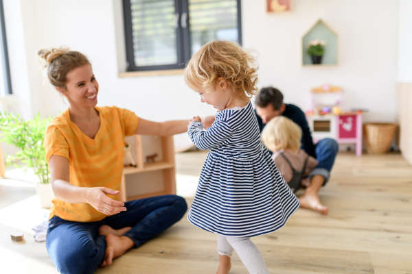 Young nuclear family playing with toys in a living room. Parents and children running, having fun, spending weekend day indoors.