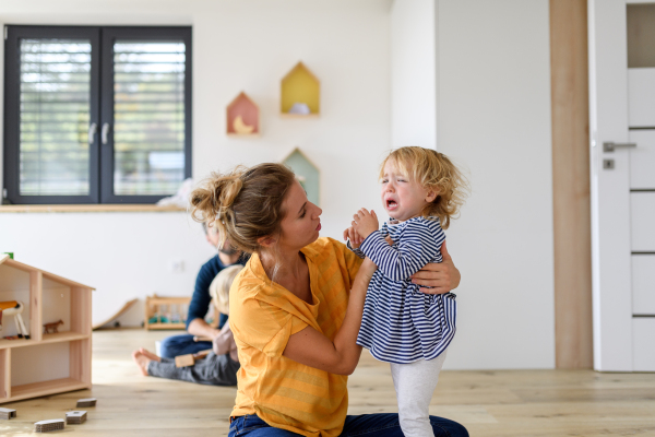 Little girl crying and screaming, mother holding her in arms, soothing her.