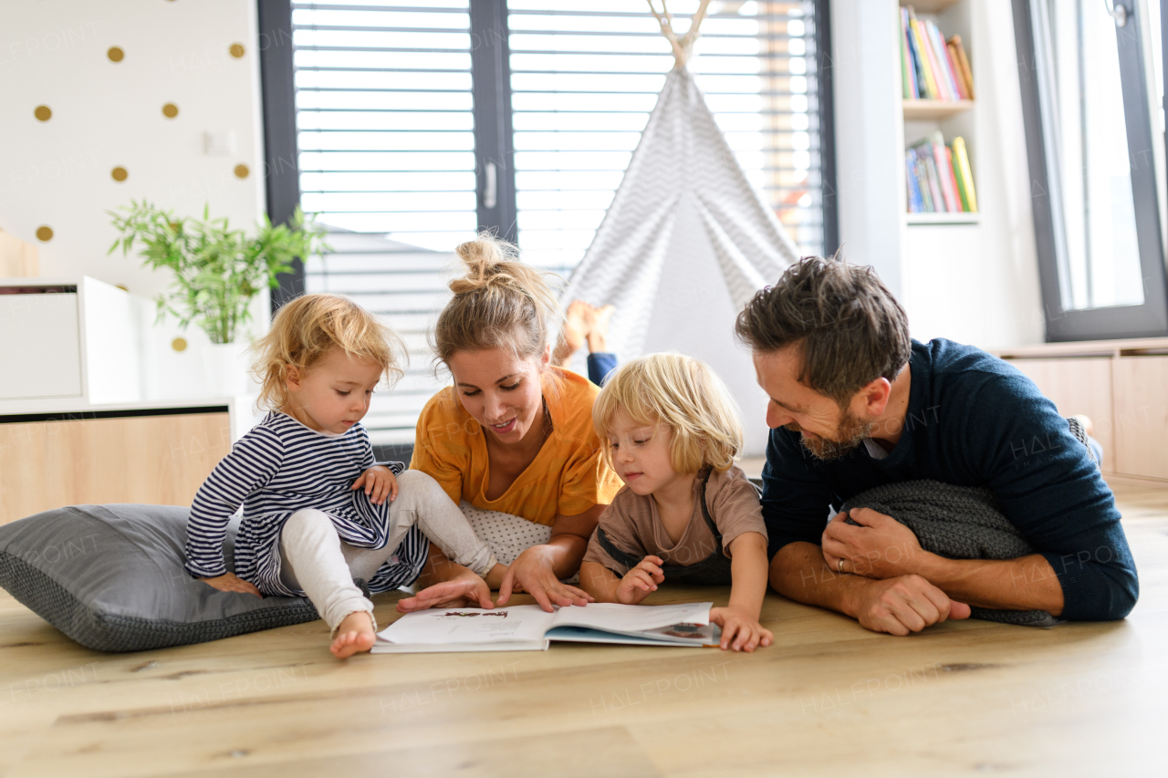 Young nuclear family playing with toys in a living room. Parents and children lying on floor, looking at children's story, picture book, spending weekend day indoors.