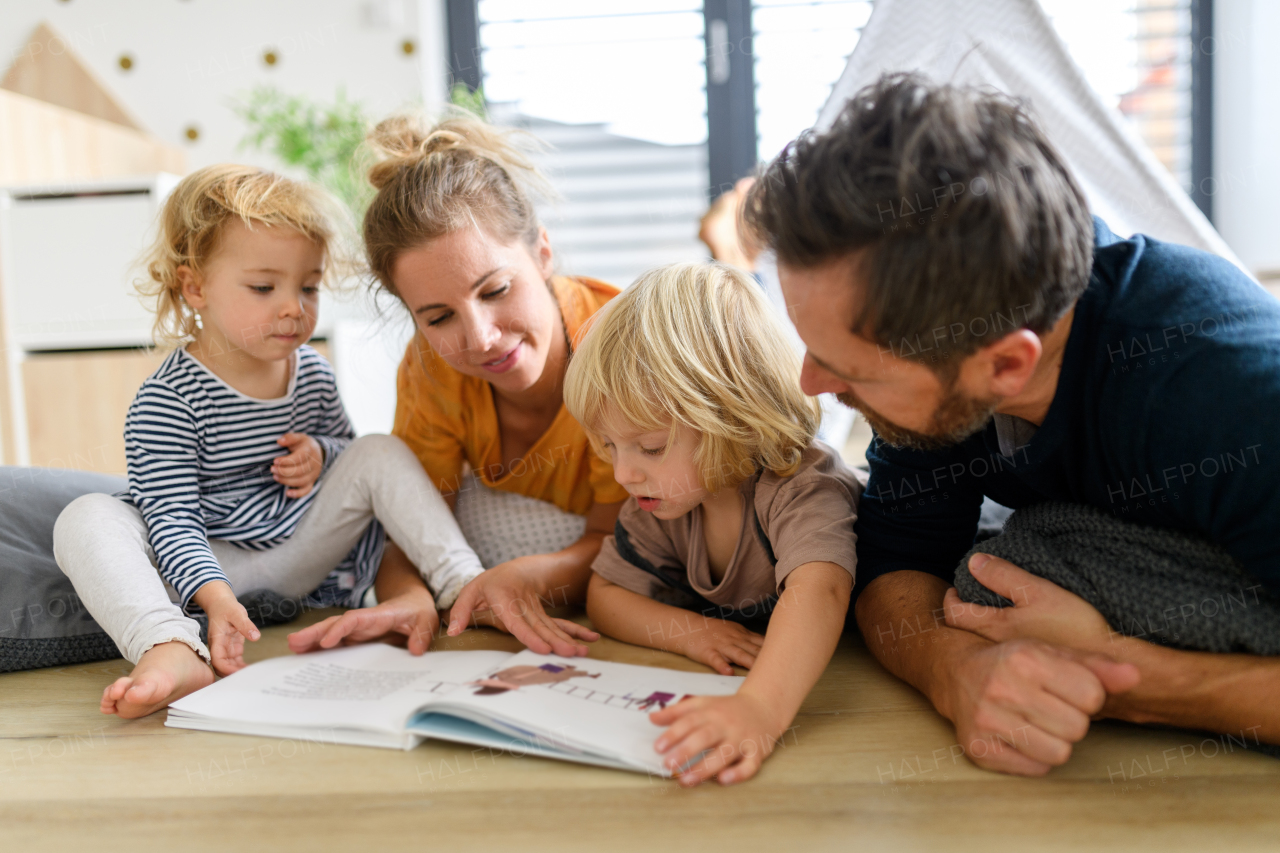 Young nuclear family playing with toys in a living room. Parents and children lying on floor, looking at children's story, picture book, spending weekend day indoors.