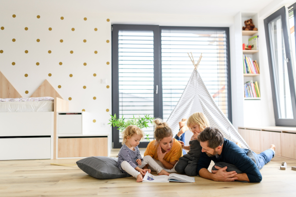 Young nuclear family playing with toys in a living room. Parents and children lying on floor, looking at children's story, picture book, spending weekend day indoors.