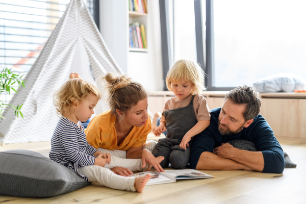 Young nuclear family playing with toys in a living room. Parents and children lying on floor, looking at children's story, picture book, spending weekend day indoors.