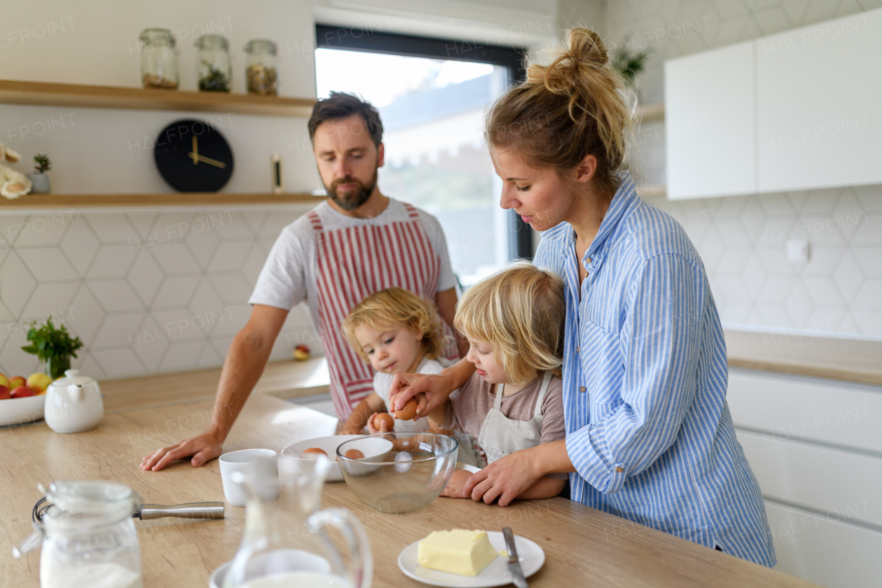 Nuclear family making pancakes together. Parents and children in kitchen, preparing pancake batter, spending weekend day indoors.