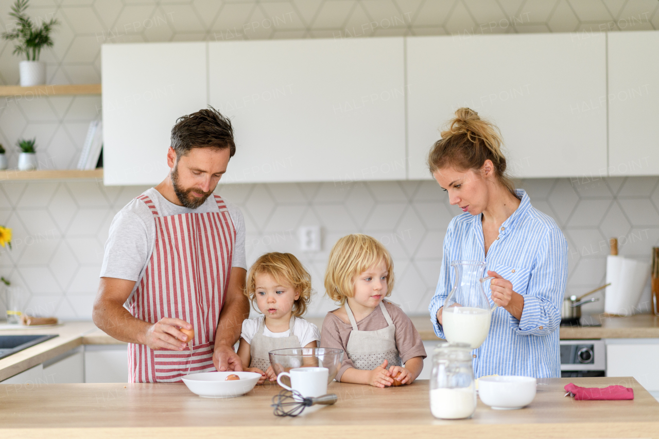 Nuclear family making pancakes together. Parents and children in kitchen, preparing pancake batter, spending weekend day indoors.