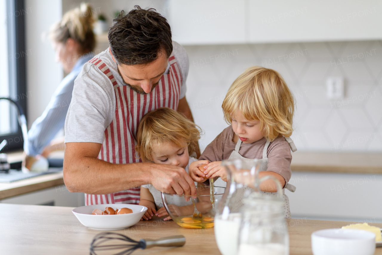 Nuclear family making pancakes together. Parents and children in kitchen, preparing pancake batter, spending weekend day indoors.