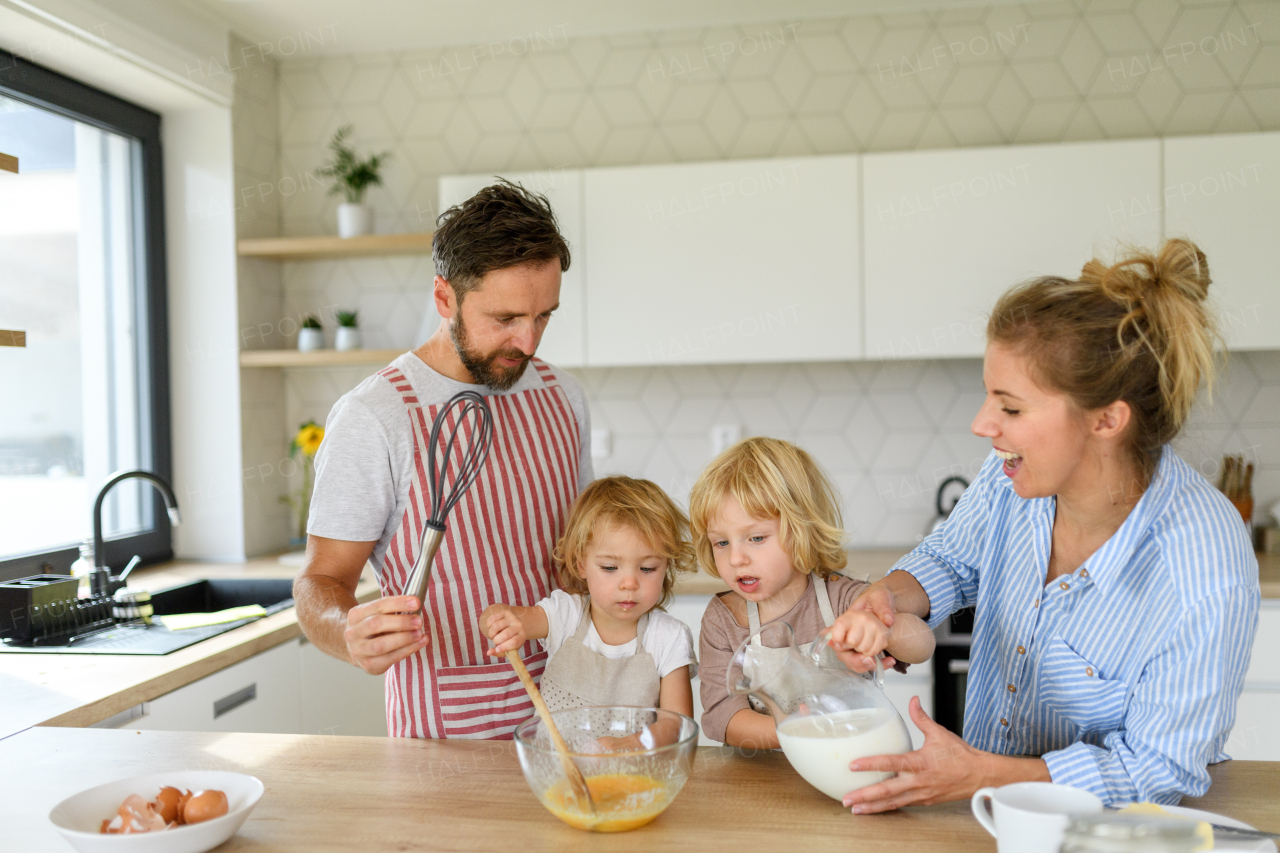 Nuclear family making pancakes together. Parents and children in kitchen, preparing pancake batter, spending weekend day indoors.