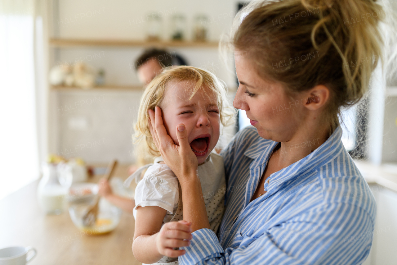 Little girl crying and screaming, mother holding her in arms, soothing her.