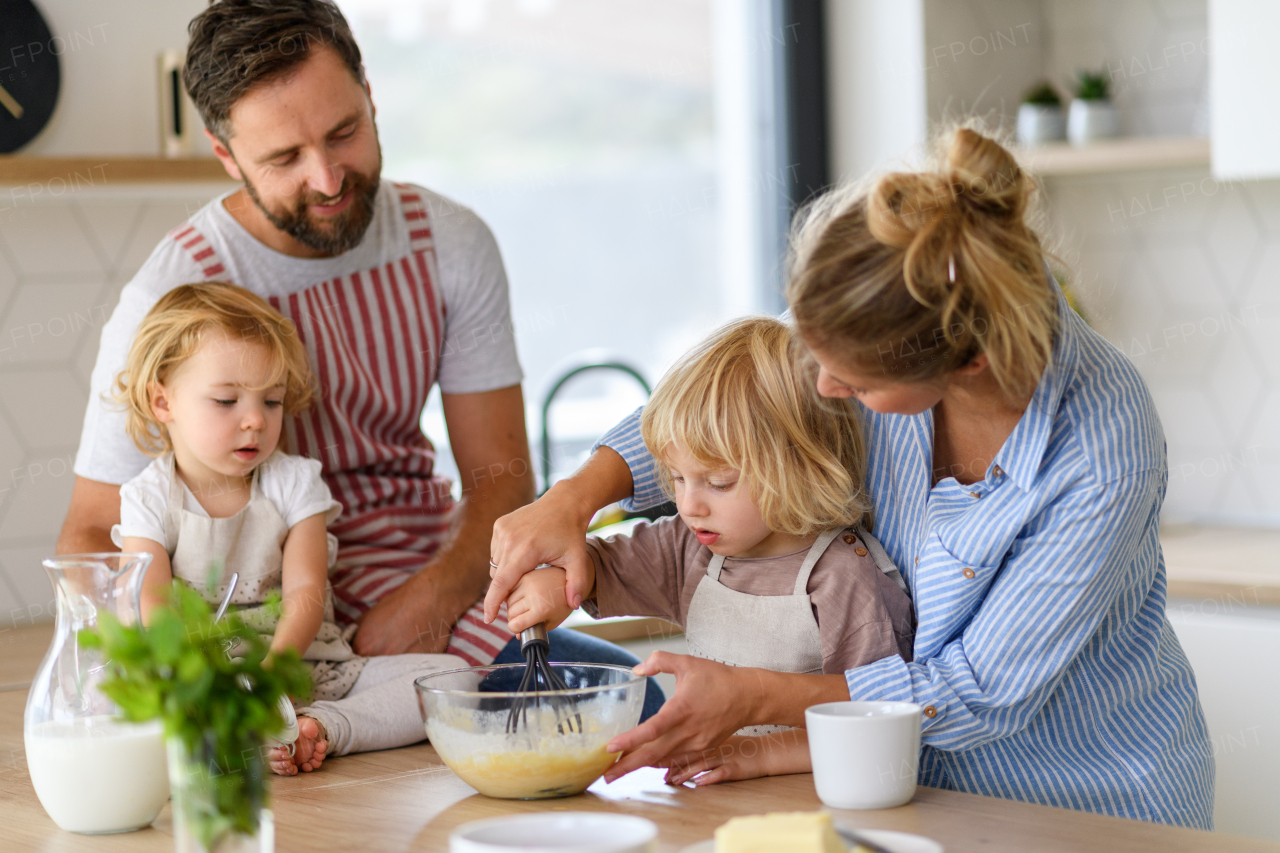 Nuclear family making pancakes together. Parents and children in kitchen, preparing pancake batter, spending weekend day indoors.