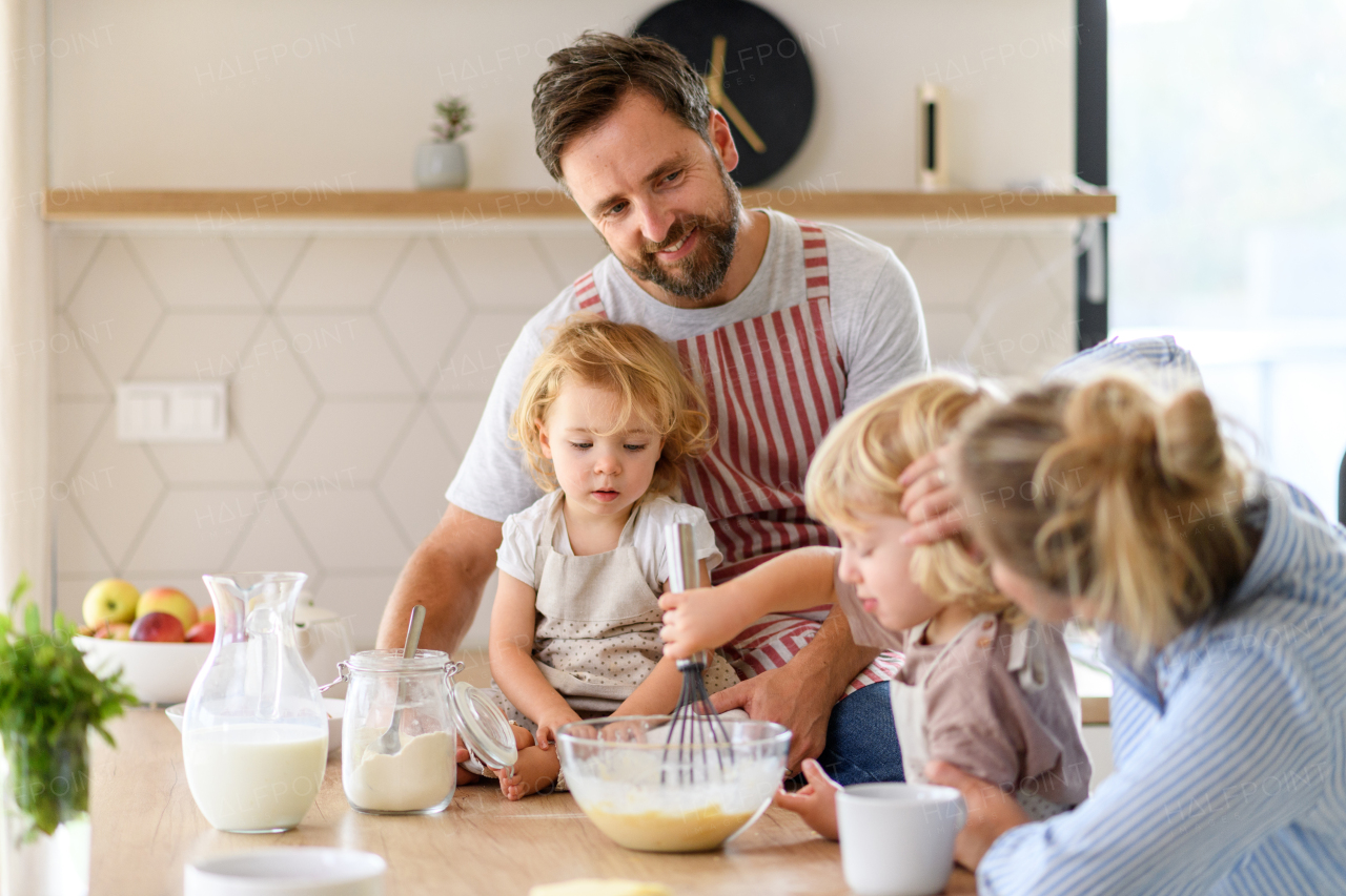 Nuclear family making pancakes together. Parents and children in kitchen, preparing pancake batter, spending weekend day indoors.