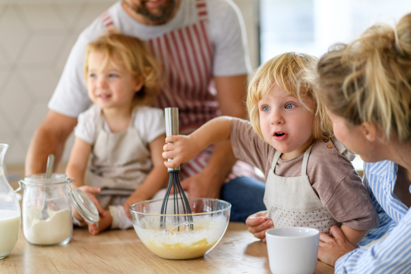 Nuclear family making pancakes together. Parents and children in kitchen, preparing pancake batter, spending weekend day indoors.