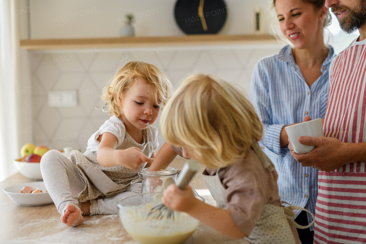 Nuclear family making pancakes together. Parents and children in kitchen, preparing pancake batter, spending weekend day indoors.