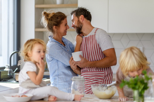 Nuclear family making pancakes together. Parents and children in kitchen, preparing pancake batter, spending weekend day indoors.