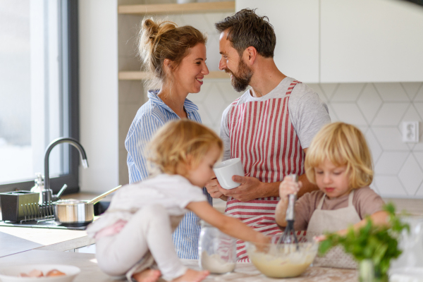 Nuclear family making pancakes together. Parents and children in kitchen, preparing pancake batter, spending weekend day indoors.