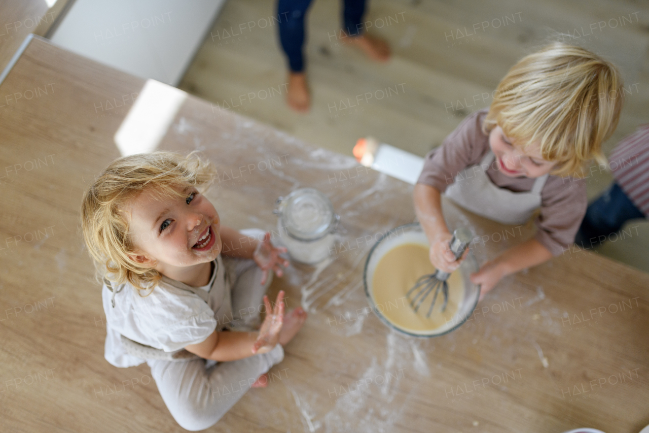 Little cute girl sitting on kitchen countertop, tasting pancake batter with finger. Nuclear family spending weekend day indoors, cooking together.